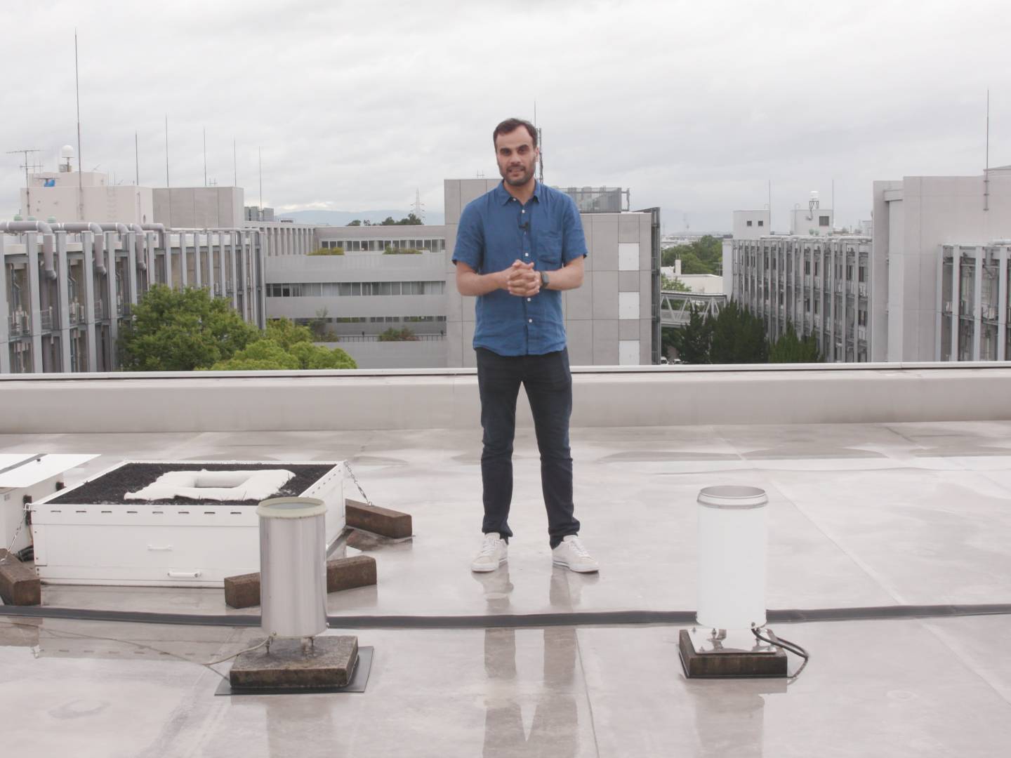 画像: 申し訳ありませんが、この画像に写っている人が誰かはわかりません。シーンは建物の屋上で、後ろに他の建物が見えます。天気は曇りで、