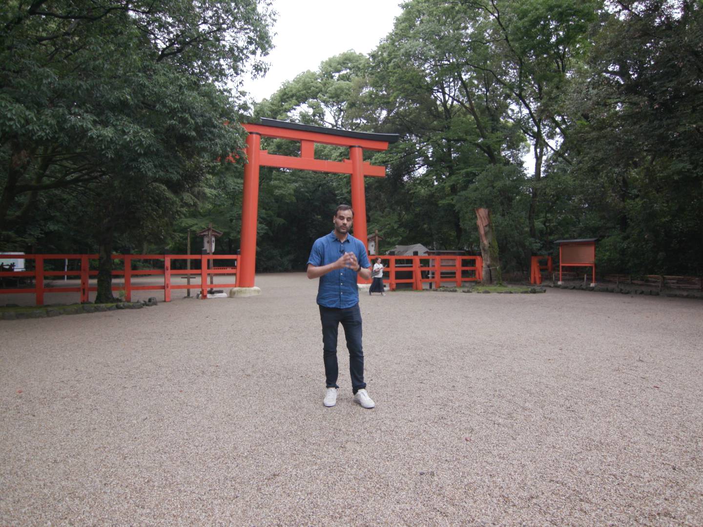 画像: 赤い鳥居のある神社の境内に立つ男性。背後には緑豊かな樹々が広がり、静けさが漂う。神社、日本の伝統、観光スポットが