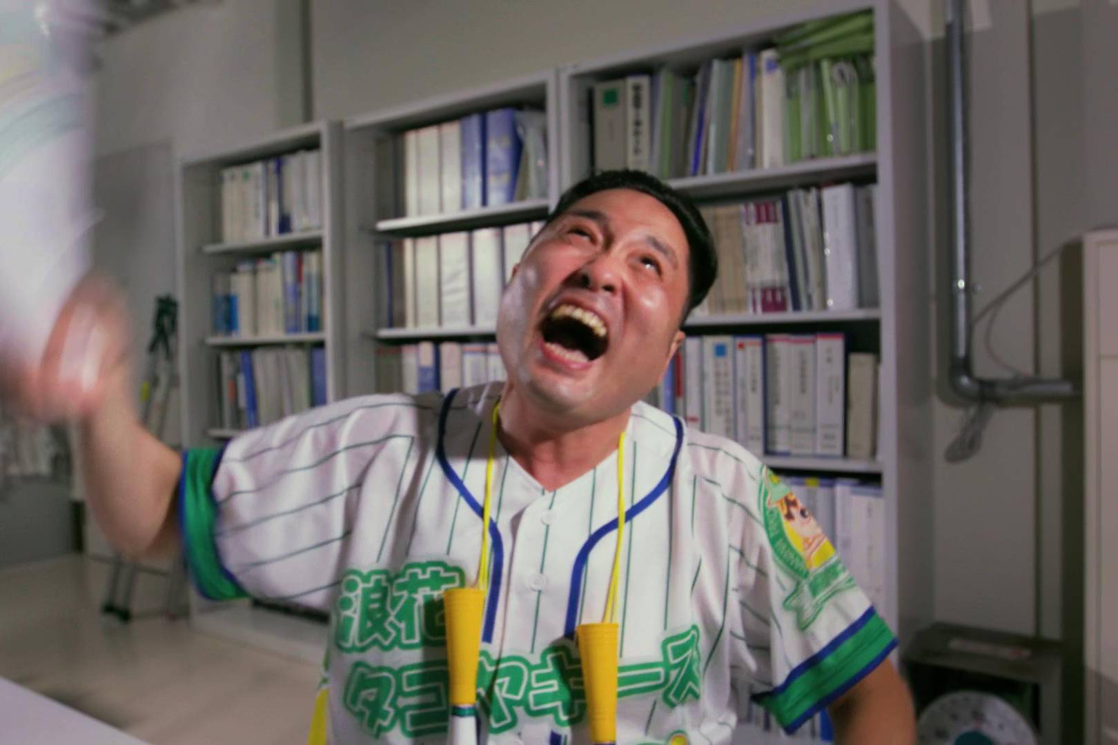 画像: 申し訳ありませんが、この画像の人を特定することはできません。しかし、オフィスのような場所でユニフォームを着た男性が何かに意気込んでいる様子が映されています。キ