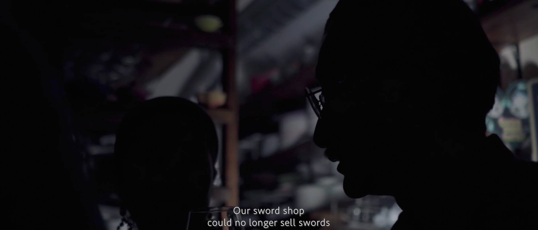 画像: 申し訳ありませんが、人物の特定はできません。この画像は、剣の販売を停止した剣の店に関する暗いシルエットのシーンです。背景にはぼんやりと店内
