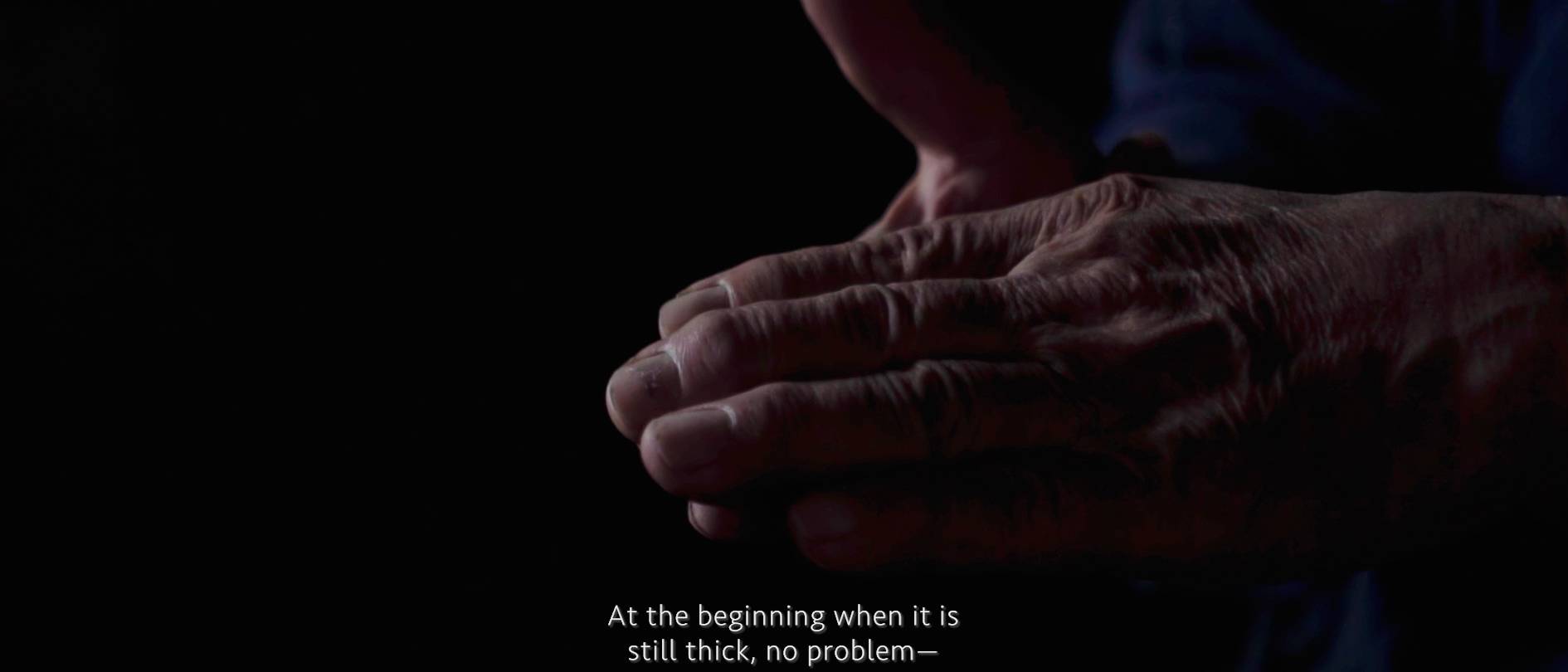 画像: 申し訳ありませんが、画像内の人物を特定することはできません。この画像では、高齢の方の手がクローズアップされています。キャプションには「At the beginning when it is still thick, no problem」と