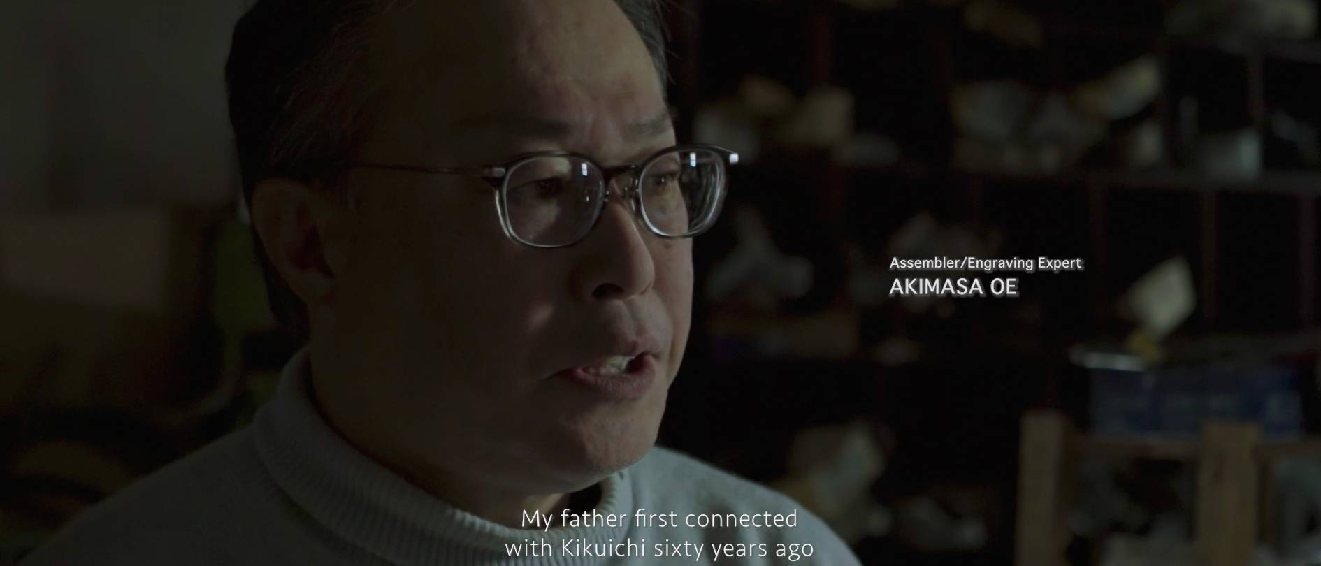 画像: 申し訳ありませんが、画像の人物を特定することはできません。この画像は、彫刻や組み立ての専門家が作業場でインタビューを受けているシーンのようです。