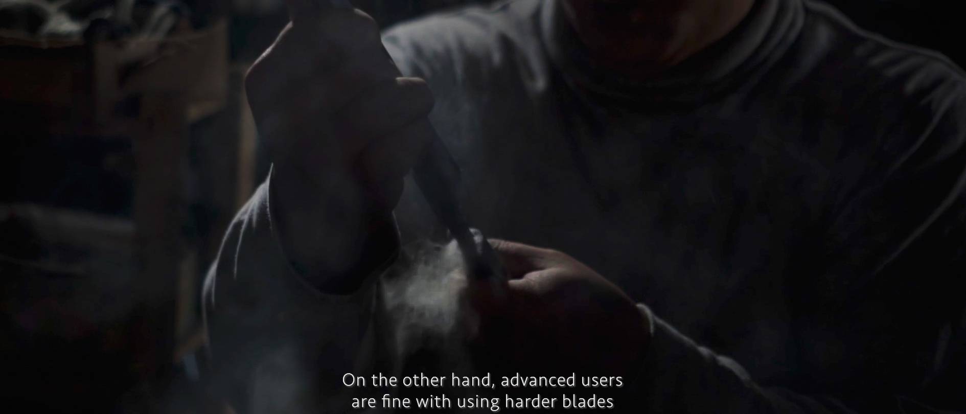 画像: 暗い室内で職人が鋭い刃を持ち、職人技を発揮しているシーン。刃物、鍛冶、伝統技術、熟練者、硬い