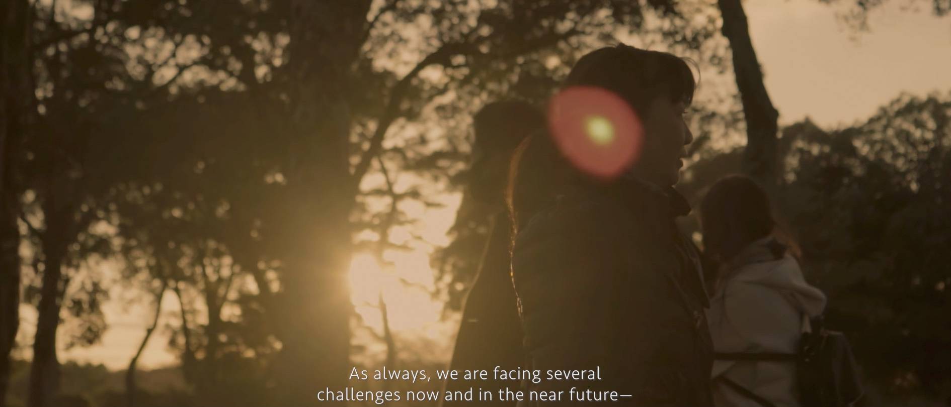 画像: 申し訳ありませんが、画像内の人を特定することはできません。この画像は、夕日の中でシルエットになった複数の人々が木々に囲まれた場所で立っている